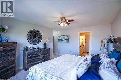 Carpeted bedroom featuring a ceiling fan with integrated lighting, a neutral wall color, and an entrance to a bathroom with a vanity and mirror - 365 Poldon Drive, Norwich, ON 