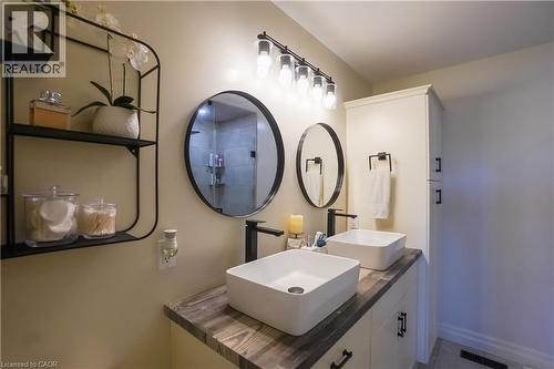 Bathroom vanity featuring dual vessel sinks, black hardware, wood-finish countertop, and integrated storage cabinetry - 365 Poldon Drive, Norwich, ON 