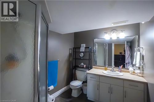 Bathroom featuring a walk-in shower with obscure glass, a single vanity with a laminate countertop, and a wall-mounted mirror with overhead lighting - 365 Poldon Drive, Norwich, ON 