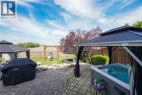 Spacious outdoor living area with a paver patio and hot tub beneath a dark-roofed gazebo - 365 Poldon Drive, Norwich, ON 