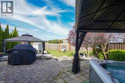 Expansive stone patio featuring a hot tub, gazebo with privacy screens, a second gazebo, established landscaping, and a manicured lawn area - 