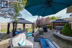 Expansive stone paver patio featuring a covered gazebo, raised garden beds, and mature landscaping - 