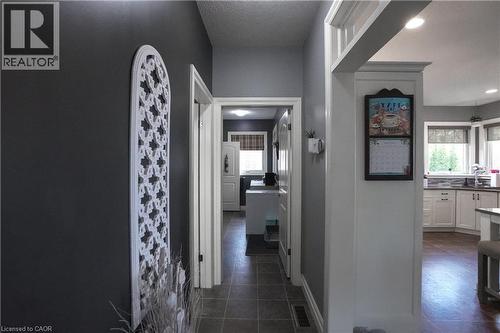 Hallway featuring dark gray walls, white trim, and tile flooring, opening to a kitchen with light cabinetry and wood-finish flooring - 365 Poldon Drive, Norwich, ON 