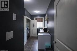 Laundry area featuring neutral-toned tile flooring, dark wall paint, and overhead lighting - 