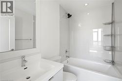 Contemporary bathroom featuring a white vanity with integrated sink, chrome faucet, a framed wall mirror, and a white bathtub with subway-tiled surround - 