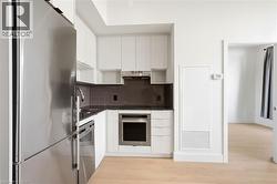 Modern kitchen featuring stainless steel appliances, dark stone countertops, white flat-panel cabinetry, and wood-finish flooring - 