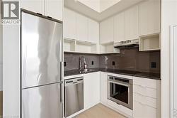 Modern kitchen featuring stainless steel appliances, dark stone countertops, a tile backsplash, light wood-finish flooring, and white cabinetry - 