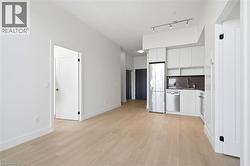 Open-concept living area featuring light wood-finish flooring, white walls, and a contemporary kitchen - 