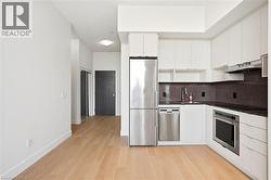 Modern kitchen featuring white cabinetry, stainless steel appliances, dark stone countertops, and a subway tile backsplash - 