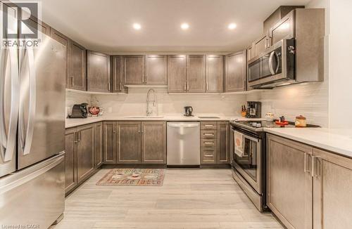 Kitchen featuring wood-finish cabinetry, stainless steel appliances, light-toned countertops, and a white subway tile backsplash - 5 Wake Robin Drive Unit# 107, Kitchener, ON 