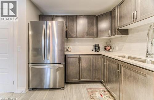 Kitchen featuring wood-finish cabinetry with modern pulls, stainless steel French door refrigerator, light-toned countertops, and a white subway tile backsplash - 5 Wake Robin Drive Unit# 107, Kitchener, ON 