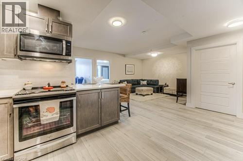 Modern kitchen featuring stainless steel appliances, wood-finish cabinetry, white tile backsplash, and light-toned countertops - 5 Wake Robin Drive Unit# 107, Kitchener, ON 