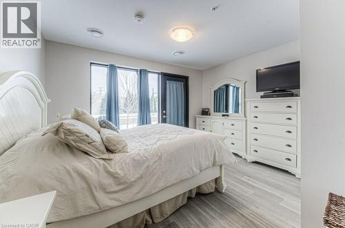 Bright bedroom featuring large windows, light wood-finish flooring, a contemporary ceiling light fixture, and recessed ceiling vents - 5 Wake Robin Drive Unit# 107, Kitchener, ON 