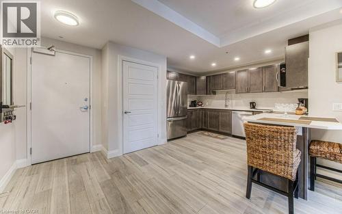 Open-concept kitchen and entry area featuring wood-finish flooring, contemporary flat-panel cabinetry, stainless steel appliances, and an eat-at counter - 5 Wake Robin Drive Unit# 107, Kitchener, ON 