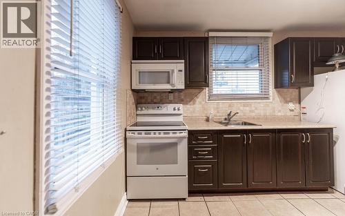 Kitchen featuring light tile patterned flooring, sink, backsplash, dark brown cabinets, and white appliances - 501 Upper Wellington Street, Hamilton, ON 