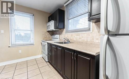Kitchen featuring sink, white appliances, decorative backsplash, and light tile patterned floors - 501 Upper Wellington Street, Hamilton, ON 