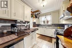 Kitchen featuring white cabinetry with brushed nickel hardware, a brick-style backsplash, and a built-in stainless steel range hood - 