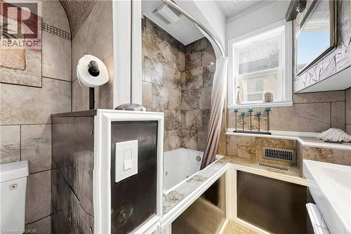 Tile-finished bathroom featuring a built-in bathtub with shower, a single window, and integrated vanity with undermount sink - 287 Courtland Avenue E, Kitchener, ON 