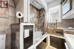 Tile-finished bathroom featuring a built-in bathtub with shower, a single window, and integrated vanity with undermount sink - 