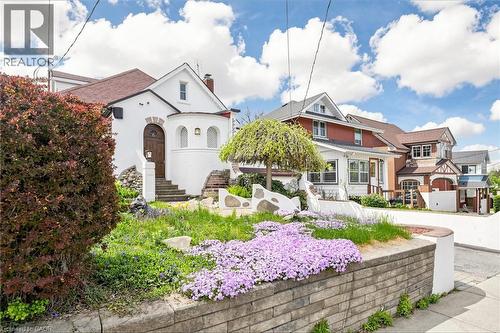Charming stucco exterior with arched entry, terraced landscaping, stone retaining wall, and mature plantings - 287 Courtland Avenue E, Kitchener, ON 