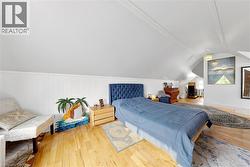 Sloping ceiling with exposed beams, wood-finish flooring, white paneled wall detailing, and a built-in window providing natural light - 