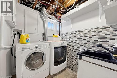 Dedicated utility space featuring a laundry sink, tile backsplash, white cabinetry, open shelving, and natural light from horizontal windows - 287 Courtland Avenue E, Kitchener, ON 