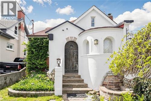 White stucco exterior with an arched wooden entry door and an arched window featuring a decorative lattice - 287 Courtland Avenue E, Kitchener, ON 