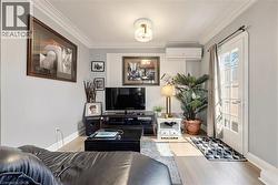 Living area featuring light wood-finish flooring, crown molding, and a built-in split air conditioning unit - 