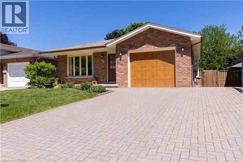 Brick exterior featuring a wood-finish garage door, paver driveway, front lawn, and mature landscaping - 12 Spartan Drive, Brantford, ON - Outdoor