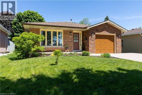 Brick exterior featuring a wood-finish garage door, a patterned paver driveway, a bay window with light-toned trim, and mature landscaping - 12 Spartan Drive, Brantford, ON - Outdoor