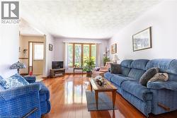Living area featuring rich wood-finish flooring, light-toned walls, and a multi-pane window with wood trim - 