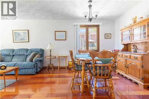Open-concept living and dining area featuring wood-finish flooring, a contemporary chandelier, light-toned wall paint, and a window with a garden view - 12 Spartan Drive, Brantford, ON - Indoor