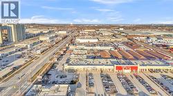 Aerial perspective highlighting a commercial corridor with multiple retail centers, a multi-lane roadway, ample surface parking, and a large multi-story residential building - 