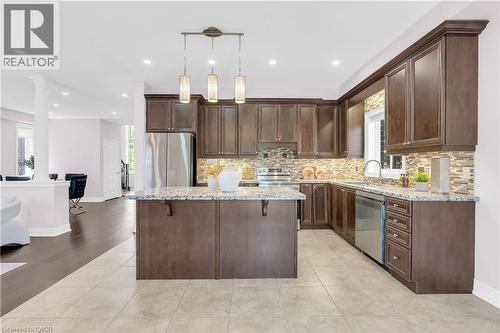 Spacious kitchen featuring dark wood cabinetry, a central island with a granite countertop, stainless steel appliances, a mosaic tile backsplash, and recessed lighting - 92 Desoto Drive, Hamilton, ON - Indoor Photo Showing Kitchen With Upgraded Kitchen