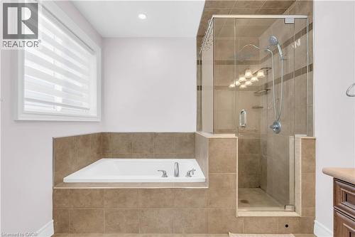 Tiled bath area featuring a built-in soaking tub with chrome fixtures, a separate glass-enclosed shower with a rainfall showerhead and handheld sprayer, and a window with horizontal blinds - 92 Desoto Drive, Hamilton, ON - Indoor Photo Showing Bathroom