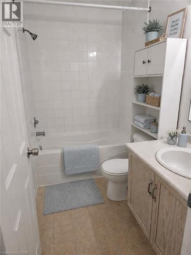 Bathroom featuring a combination shower and tub with white tile surround, a single-sink vanity with wood-finish cabinetry and light-toned countertop, a toilet, and light-toned tile flooring - 390 Wake Robin Crescent, Kitchener, ON - Indoor Photo Showing Bathroom