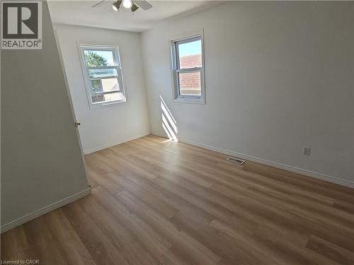 Light-filled room featuring wood-finish flooring, white walls, two windows, and a ceiling fan with integrated lighting - 390 Wake Robin Crescent, Kitchener, ON - Indoor Photo Showing Other Room