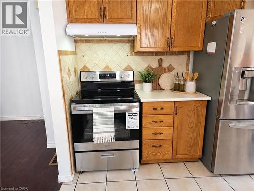 Kitchen area featuring a stainless steel range, a white range hood, light wood-finish cabinetry, a light-toned countertop, and a tiled backsplash - 390 Wake Robin Crescent, Kitchener, ON - Indoor Photo Showing Kitchen