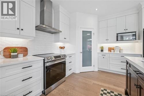 White cabinetry with matte black hardware, stainless steel appliances, light wood-finish flooring, white subway tile backsplash, and frosted glass pantry door - 30 Waterbow Trail, Kitchener, ON - Indoor Photo Showing Kitchen With Upgraded Kitchen