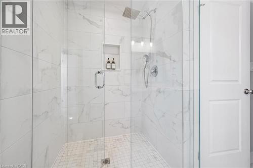 Glass-enclosed shower featuring large format white tile walls with subtle veining, a rain shower head, a handheld shower fixture, and an integrated tiled niche - 30 Waterbow Trail, Kitchener, ON - Indoor Photo Showing Bathroom