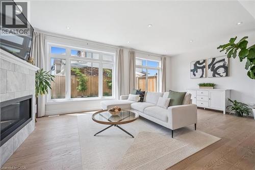 Spacious living area featuring large windows, wood-finish flooring, recessed lighting, a tiled fireplace surround, and white baseboards - 30 Waterbow Trail, Kitchener, ON - Indoor Photo Showing Living Room With Fireplace