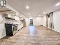 Open-concept living space featuring wood-finish flooring, a full kitchen with stainless steel appliances, recessed lighting, and a neutral color palette - 