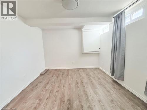 Open room featuring wood-finish flooring, white painted walls, and a flush-mount ceiling light fixture - 11 Duncairn Avenue, Kitchener, ON 