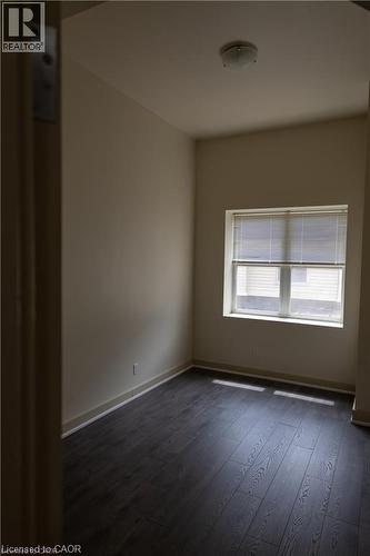 Room featuring dark wood-finish flooring, light neutral-toned walls, a single window with blinds, and an overhead flush-mount light fixture - 365 Colborne Street, Brantford, ON 