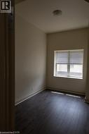 Room featuring dark wood-finish flooring, light neutral-toned walls, a single window with blinds, and an overhead flush-mount light fixture - 