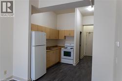 Kitchenette featuring light wood-finish cabinetry, a white refrigerator, a white electric range, and dark wood-finish flooring - 