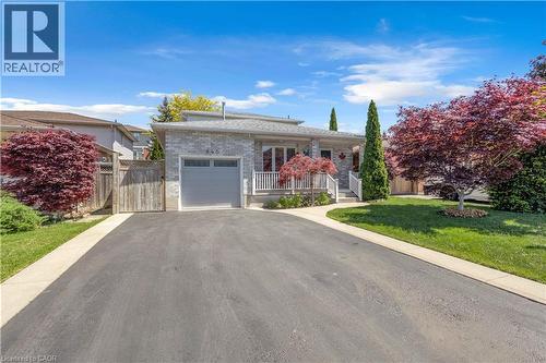 Stone-clad exterior featuring a light gray garage door, a front porch with white railings, and a paved driveway - 640 Acadia Drive, Hamilton, ON 