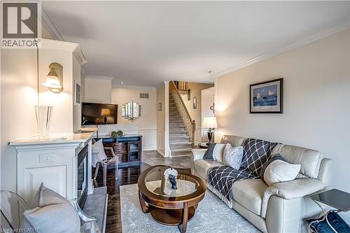 Living room featuring a fireplace with white mantel, dark wood-finish flooring, staircase with carpeted treads and wood banister, and crown molding - 640 Acadia Drive, Hamilton, ON 