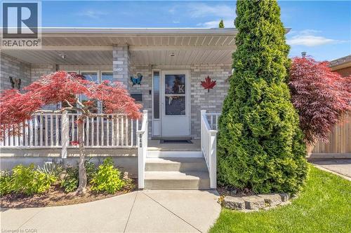 Brick exterior featuring a covered porch with white railing, concrete steps, and a landscaped front yard with mature trees - 640 Acadia Drive, Hamilton, ON 
