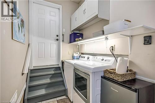 Dedicated laundry area featuring a washer and dryer, upper cabinetry, shelving, and a paneled entry door - 640 Acadia Drive, Hamilton, ON 